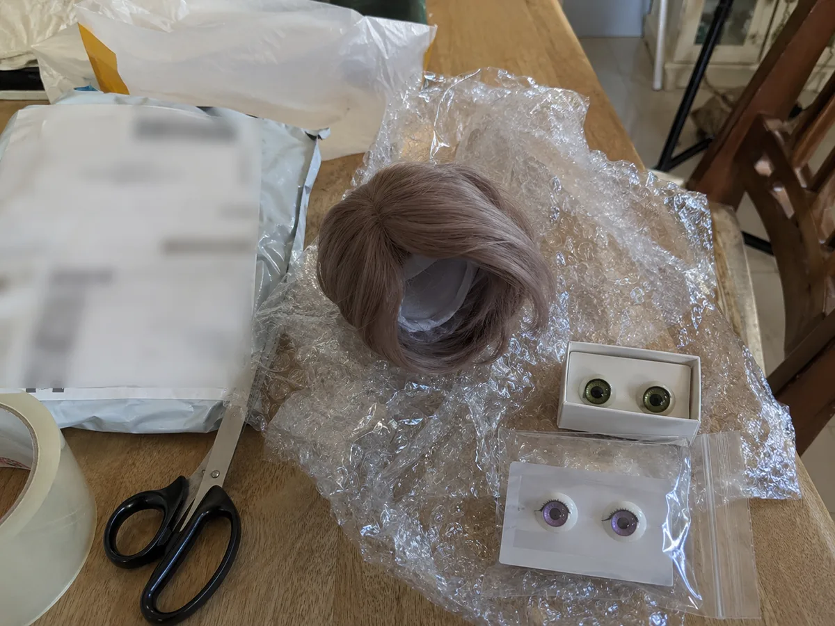 Small parcel table check: Small package opened on a regular table with scissors, bubble wrap, wig, and eye accessories.